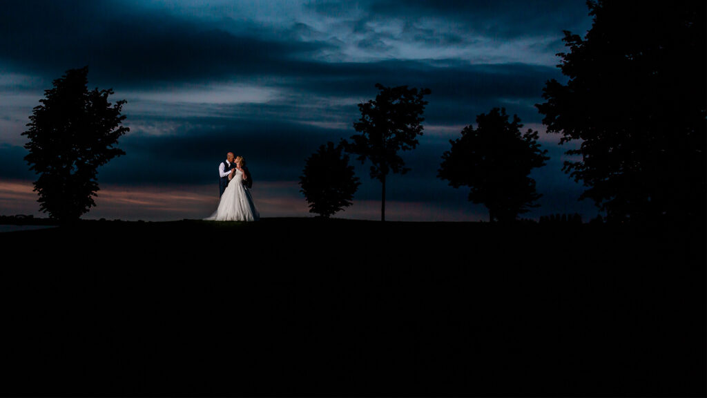 Bruidsfoto van een stralend bruidspaar dat elkaar liefdevol aankijkt, met een prachtige achtergrond vol natuurlijke kleuren die de romantische sfeer van de trouwdag benadrukt.